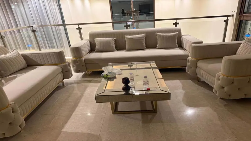 Large beige majlis sofa set with matching armchairs and a mirrored coffee table